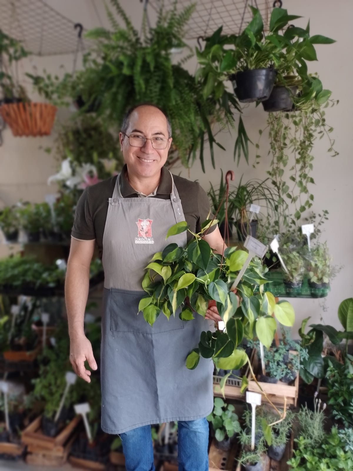 Edu na Rosa e Cia, segurando uma planta entre as flores da loja